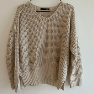 Beige stickad tröja - Säljer en mysig beige stickad tröja med v-ringad design och långa ärmar med ribbade muddar. Stickad med större maskor, luftig och skön. Så snygg till ljusa eller vita jeans. One size.