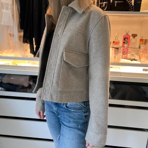 Beige jacka med knappar - Snygg beige jacka med knappar framtill. Jackan har en praktisk ficka med lock på bröstet. Passar bra till jeans och andra vardagsplagg.