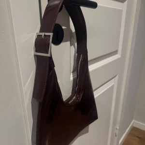 Vinröd axelväska med spänne - Brun/ rödvinsfärgad axelväska med spänne.  Knappt använd från Carin Wester