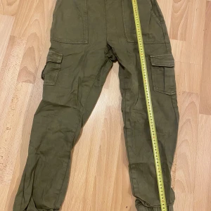 Olivgröna cargobyxor från KappAhl - Snygga olivgröna cargobyxor från KappAhl i storlek XS. Byxorna har flera praktiska fickor och är tillverkade i 100% bomull för en bekväm passform. Perfekta för en avslappnad stil.