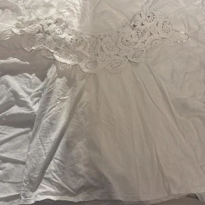 Vit blus med spetsdetaljer - Säljer en vacker vit blus med fina spetsdetaljer upptill. Klänningen har en elegant design som passar perfekt för somriga tillfällen. Den är ärmlös och har en luftig passform som ger en skön känsla. Perfekt för dig som vill ha en stilren och romantisk look.