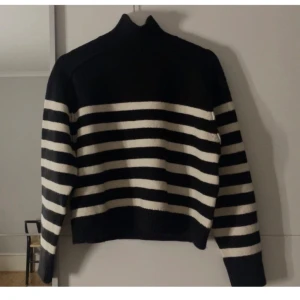 Svart och vit randig polotröja - Säljer en snygg svart och vit randig polotröja med långa ärmar. Tröjan har en hög krage och är perfekt för kyligare dagar. Den är både stilren och bekväm. Oanvänd