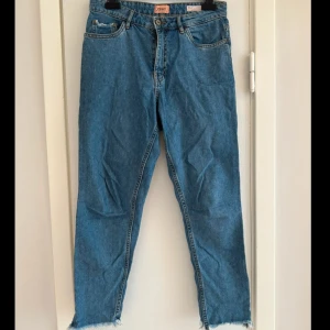 Blå jeans från ONLY - Snygga blå high-waisted mom jeans från ONLY. De har en klassisk femficksdesign och råa kanter vid bensluten för en trendig look. Perfekta för en avslappnad stil.  Storlek: 28/32  Ben 66 cm  Midja ca 74 cm