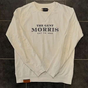 Vit tröja från Morris - Säljer en stilren vit tröja från Morris med texten 'The Gent Morris EST TM 1968' på framsidan. Tröjan är tillverkad i 100% bomull och har långa ärmar samt ribbade muddar vid ärmslut och nederkant. Perfekt för en avslappnad look.