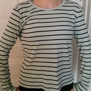 Randig långärmad tröja - Säljer en stilren randig tröja med långa ärmar. Tröjan har en ljus bas med svarta ränder och en rund halsringning. Perfekt för en avslappnad stil💕