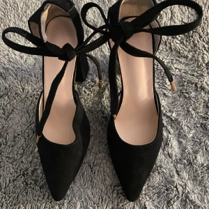 Svarta klackskor med knytband - Eleganta svarta klackskor med spetsig tå och knytband runt ankeln. Skorna har en hög klack och är tillverkade i ett material som liknar mocka. Perfekta för en stilren look. Använda en gånga endast inomhus🤍🌟