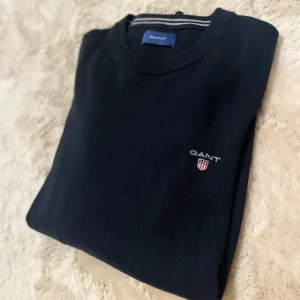 Svart tröja från GANT - Säljer en stilren svart tröja från GANT med rund hals och diskret logotyp på bröstet. Perfekt för en klassisk look.
