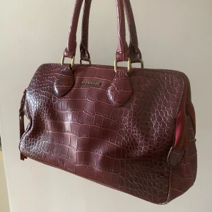 Vintage röd handväska  - Denna fina väskan används tyvärr inte.  Den har 3 stora fack(bild 3), alla med flera innerfack. Det finns även ett ytterfack på utsidan. Har lite små defekter på flätorna på dragkedjorna(bild 4) men övrigt i gott skick. Medkommer axelrem(bild 5)!!