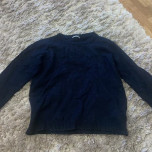 Mörkblå stickad tröja - Säljer en mysig mörkblå stickad tröja. Perfekt för kyliga dagar med sin varma och bekväma passform. Tröjan har långa ärmar och en klassisk rund halsringning. Passar både till vardags och lite finare tillfällen.