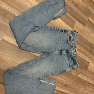 Ljusa jeans med slitna detaljer - Säljer ett par ljusa jeans med en avslappnad och sliten look. De har en rak passform men slits nertill och är tillverkade i klassiskt denimtyg. Perfekta för en casual stil!
