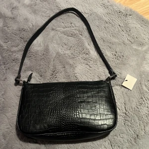 väska - säljer denna oanvända svarta väskan från stocholms accessoarer. den är köpt för 499kr säljer för 300kr. den är helt oanvänd. den har en zipficka samt mindre fickor.