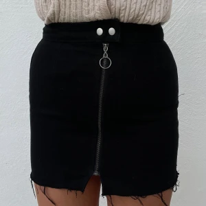 Svart kjol med dragkedja - Säljer en superfin svart kjol med en cool dragkedja framtill. Den har en rå kant nertill som ger en lite edgy look. Perfekt för både vardag och fest! 🖤