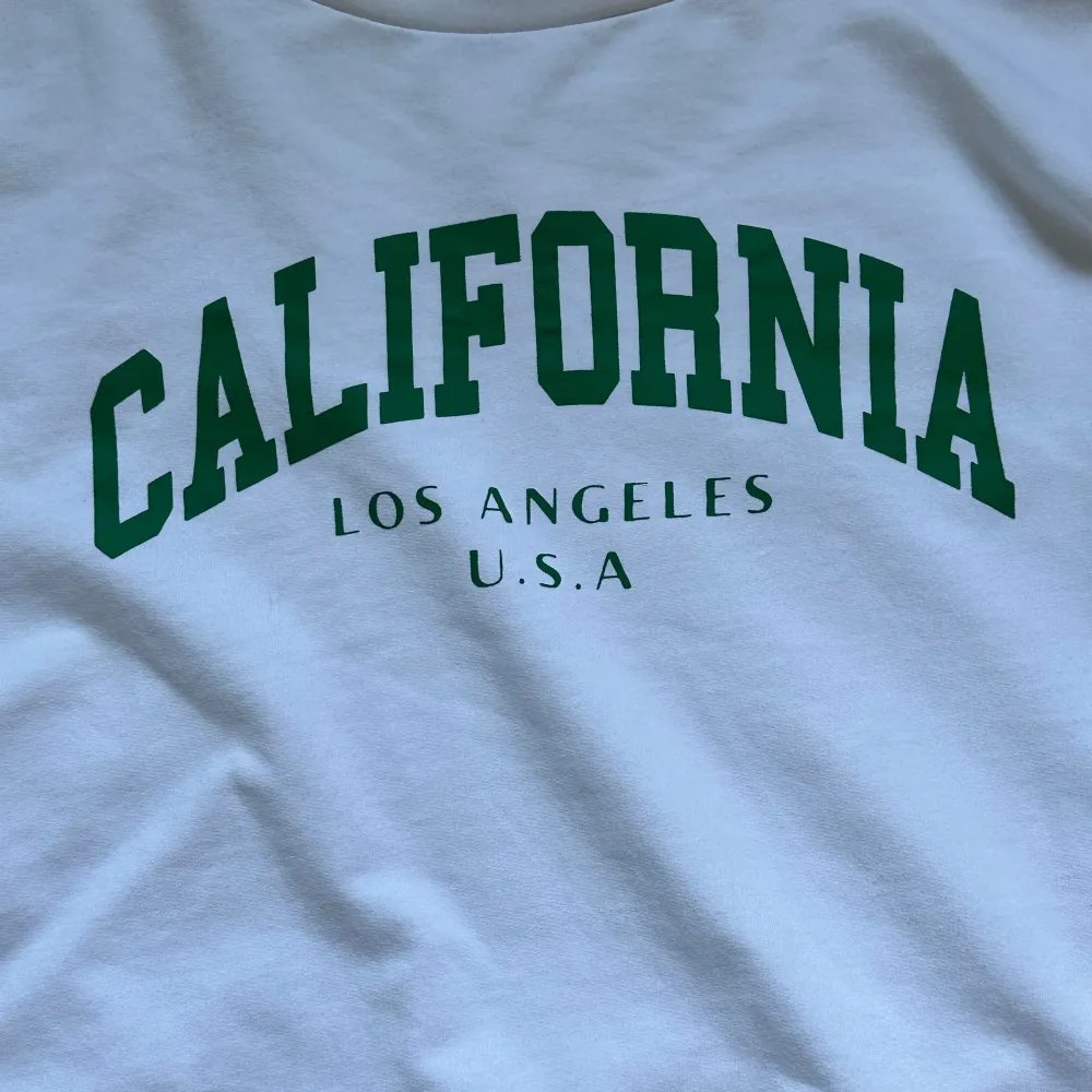 Säljer en vit sweatshirt med grönt tryck 'California Los Angeles U.S.A'. Den är superbekväm och perfekt för en avslappnad stil. Tröjan har långa ärmar och en normal passform. Perfekt för höst och vår!. Tröjor & Koftor.