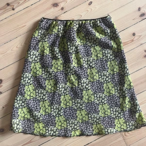 Blommig kjol från Joy - Säljer en superfin blommig kjol från Joy i storlek 40. Kjolen har ett härligt mönster med små blommor i svart, vitt och limegrönt. Perfekt för vår och sommar! Den är i ett lätt och bekvämt material, perfekt för varma dagar.