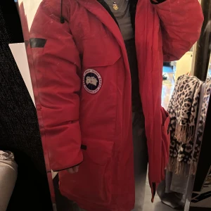 Röd parkajacka från Canada Goose - Säljer en supervarm och snygg röd parkajacka från Canada Goose. Den har en fluffig pälsluva och är perfekt för kalla vinterdagar. Jackan har långa ärmar och en praktisk dragkedja. Den passar både till killar och tjejer unisex. självklart Äkta