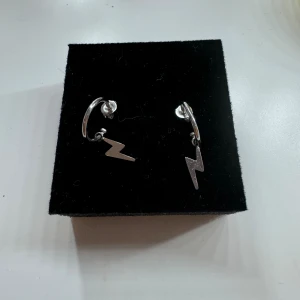 Coola blixtformade örhängen i silver - Säljer ett par riktigt coola örhängen i silver med blixtformade hängen. Perfekta för att ge din outfit en edgy touch! De är i nyskick och har en enkel men stilren design som passar till både vardag och fest. Köp dem nu och blixtsnabbt uppgradera din smyckeskollektion ⚡