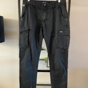 Svarta cargopants från Blend - Säljer ett par svarta cargopants från Blend i storlek 31/34. Byxorna har flera praktiska fickor, inklusive två stora fickor på sidorna. De är tillverkade i ett slitstarkt material och har en bekväm passform. Perfekta för vardagsbruk eller utomhusaktiviteter.