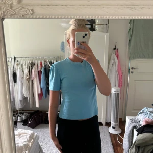 Ljusblå t-shirt - Säljer en ljusblå t-shirt i bomull. Den är kortärmad och har en tight passform. Perfekt för sommaren eller som en baströja till vardags. Skön och enkel att matcha med olika outfits.