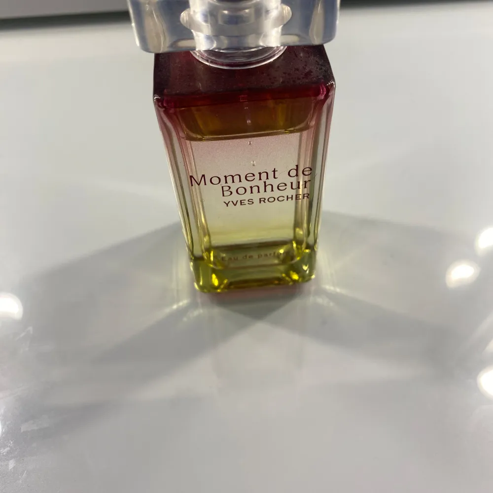 Säljer en elegant parfymflaska av Moment de Bonheur från Yves Rocher. Flaskan har en vacker gradient design som går från rött till grönt, vilket ger den ett lyxigt utseende. Parfymen är en Eau de Parfum, vilket innebär att den har en högre koncentration av doftoljor och därmed varar längre på huden. Perfekt för både dag- och kvällsanvändning. Köp direkt eller ge prisförslag 💛. Parfym.