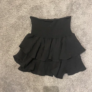 Svart volangkjol - Säljer en superfin svart volangkjol som är perfekt för både vardag och fest. Kjolen har en hög midja och flera lager av volanger som ger en snygg och lekfull look. Den är i nyskick och passar perfekt till en enkel topp eller en mer dressad blus. Perfekt för alla säsonger!