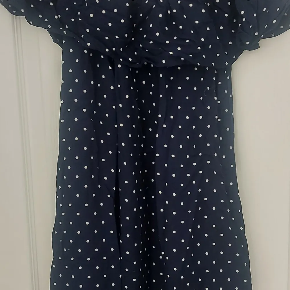 Säljer en superfin mörkblå klänning med vita prickar. Klänningen är perfekt för sommarens alla fester och har en söt offshoulder-design. Den är i nyskick och passar perfekt för en dag på stan eller en kväll ute. Materialet känns lätt och luftigt, vilket gör den bekväm att bära hela dagen.. Mekot.