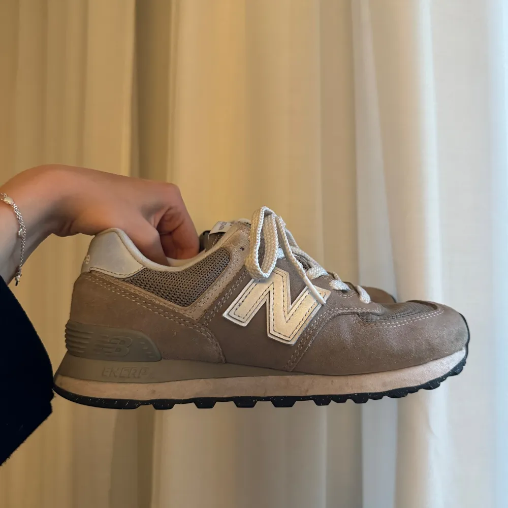 Säljer ett par beigea sneakers från New Balance i modellen 574. Skorna har tecken på användning men är i bra skick!. Skor.