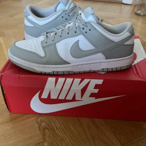Nike Dunk Low Grey Fog - Säljer ett par Nike Dunk Low sneakers i grått och vitt. Skorna är i nyskick och kommer med originalkartong. De har en klassisk design med snörning och är perfekta för både vardag och träning. 