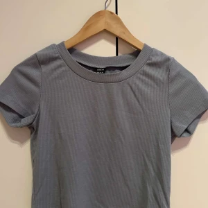 Grå ribbad t-shirt från H&M - Säljer en stilren grå ribbad t-shirt från H&M. Den har en rund halsringning och korta ärmar, perfekt för en avslappnad look. Passar bra till jeans eller kjol. Hör av dig vid intresse!
