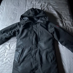 Svart parkajacka från Canada Goose - Tjaa! Säljer en canada goose jacka jag haft ett tag nu den är ganska använd å passar inte mig längre den är lite sliten mitten knapparna finns inte de e bara den högst upp å längst ner som är kvar och den hade behövt kemtvättas den är äkta men säljer den billigt hör av er vid frågor elr nåt 
