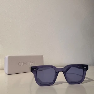 Lila solglasögon från Chimi - Snygga lila solglasögon från Chimi med en fyrkantig form. De har en transparent lila båge och matchande lila linser. Perfekta för att ge din stil en färgklick!