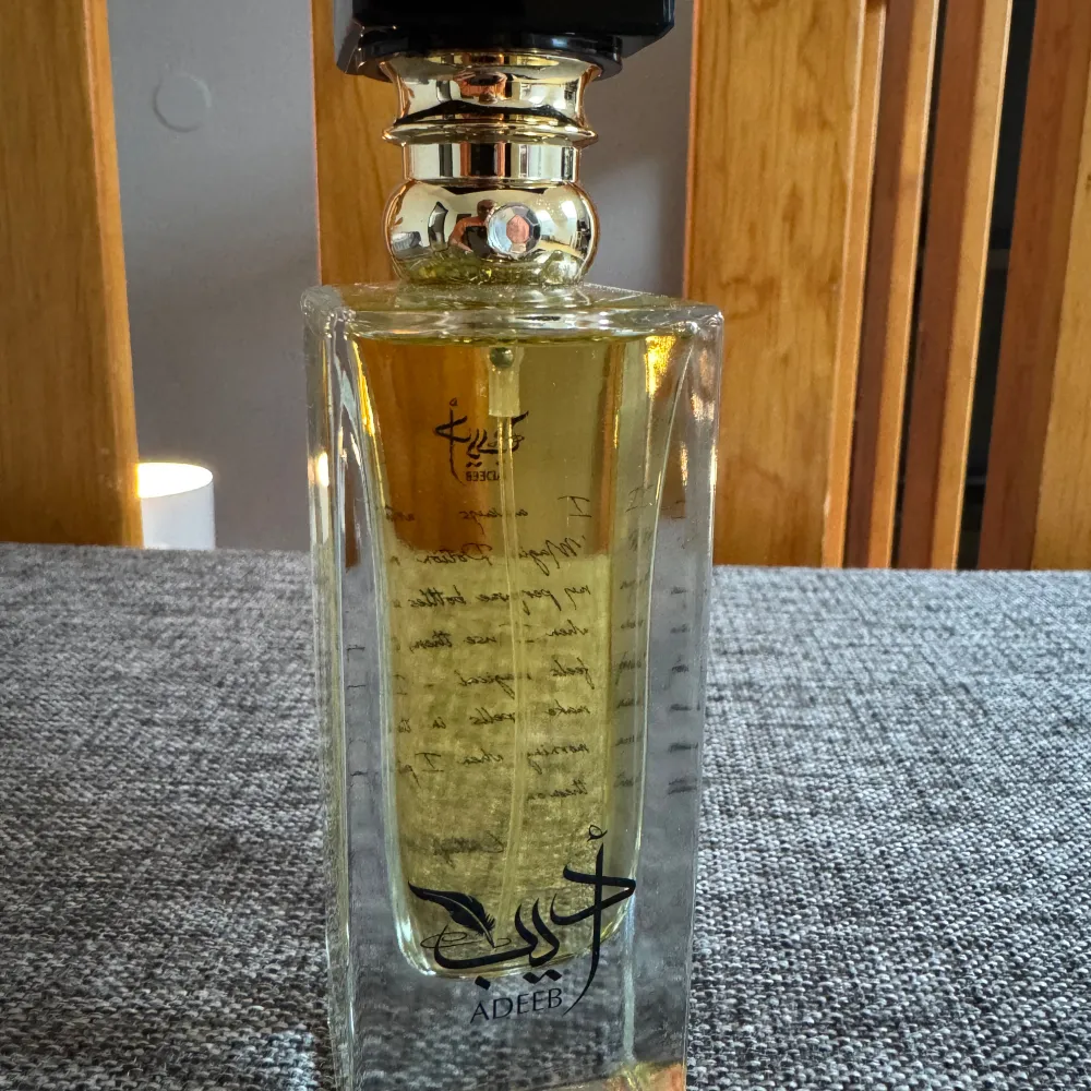 Elegant parfymflaska med en gyllene vätska från märket Adeeb. Flaskan har en fyrkantig form med en svart och guld kork som ger en lyxig känsla. Perfekt för den som söker en unik doftupplevelse. Endast testad. Förpackning saknas.. Perfume.