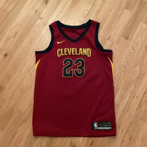Cleveland Cavaliers Tränings Linne (Lebron James) - Säljer nu mitt röda Linne med gula och blåa detaljer som jag köpte på en basket match i USA, nummer 23 på ryggen vilket indikerar spelarnumret av Lebron James. Högsta kvalitet av basket linnen man kan få tag på, kvitto finns ej då varan köptes i USA 2014 men har knappt används sen dess. Nypris var cirka 180$!