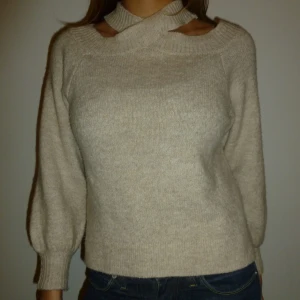 Beige stickad tröja med unik halsdesign - Cool, beige stickad tröja med en unik korsad halsdesign. 😮❣️Denna design gör att du kan bära tröjan på olika sätt. Off shoulder etc. Med denna sticker du garanterat ut🤩