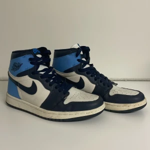 Nike Air Jordans 1 i blått och vitt - Snygga Nike Air Jordans i en fräsch kombination av ljus och mörk blått. Skorna har en hög siluett med klassisk snörning och den ikoniska Nike-loggan på sidan. 