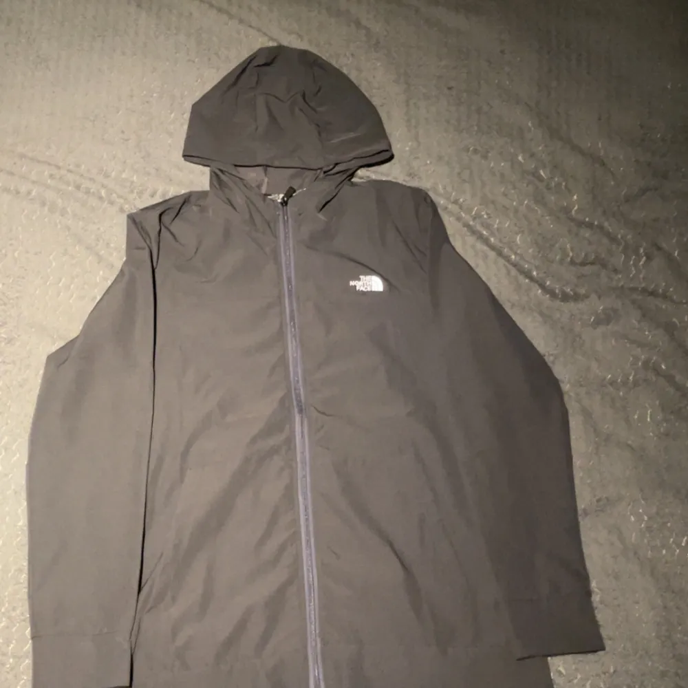Säljer en stilren svart vindjacka från The North Face. Jackan har en praktisk huva och dragkedja framtill. Perfekt för blåsiga dagar och har en diskret logga på bröstet. Passar bra för utomhusaktiviteter och vardagsbruk.. Takit.