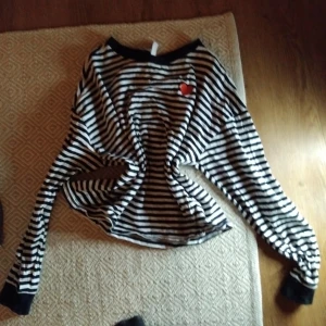 Randig långärmad tröja med hjärtdetalj - Säljer en svartvit randig långärmad tröja med en söt röd hjärtdetalj på bröstet. Tröjan har en avslappnad passform och svarta muddar vid ärmslut och halsringning. Perfekt för en casual look! kontakta mig vid frågor om mer bilder, mått, pris osv🥰