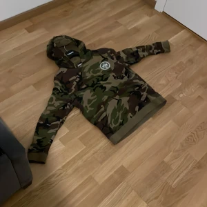Camouflage hoodie från Vans pris kan diskuteras dock - Säljer en cool camouflage hoodie från Vans med stor logga på ryggen. Tröjan har en klassisk huva och långa ärmar, perfekt för en avslappnad stil. Den är i en grön och brun färgskala som ger en tuff look. Passar perfekt för streetwear-entusiaster.