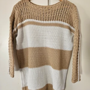 Beige och vit randig stickad tröja - Säljer en snygg beige och vit randig stickad tröja med tre-kvartsärmad design. Tröjan är tillverkad av 50% bomull och 50% akryl, vilket gör den både bekväm och stilren. Perfekt för en avslappnad look.  Djur och -rökfritt hem.