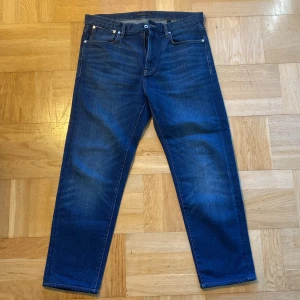 Blå jeans från John Varvatos - Snygga blå jeans från John Varvatos med klassisk femficksdesign och knappgylf. Perfekta för en stilren look med en rak passform och subtila detaljer. Märkeslappen i läder baktill ger en exklusiv touch. Aldrig använda, nypris 3000kr. W33, dom är lite korta i längden, skulle uppskatta typ L30. 