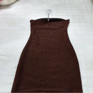Brun glittrig klänning - Snygg brun glittrig klänning med en tight passform. Perfekt för en kväll ute med vänner. Axelbandslös design som ger en elegant look.