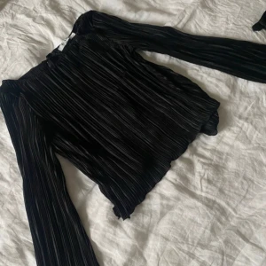 Svart plisserad blus - Elegant svart plisserad blus med långa vida ärmar och knytband baktill 