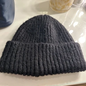 Svart ribbad mössa från Wera - Säljer en stilren svart ribbad mössa från Wera. Perfekt för kyliga dagar med sin mjuka och varma design. Mössan har en klassisk passform och är enkel att matcha med olika outfits. Mössan är aldrig använd!