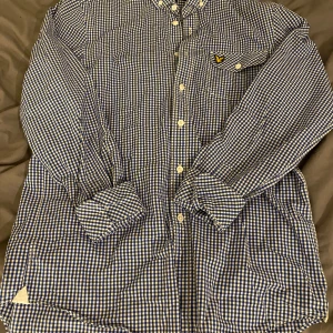 Blårutig skjorta från Lyle & Scott - Säljer en stilren blårutig skjorta från Lyle & Scott i storlek M. Skjortan har långa ärmar och en klassisk krage. Den är försedd med knappar och en bröstficka med en broderad logotyp. Perfekt för en avslappnad men ändå uppklädd look. Det är en vintage modell