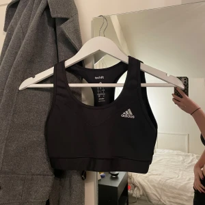 Svart sporttopp från Adidas - Säljer en svart sporttopp från Adidas med techfit och climalite-teknologi. Toppen har en brottarrygg och är perfekt för träning. Adidas-loggan är tryckt på framsidan. No support
