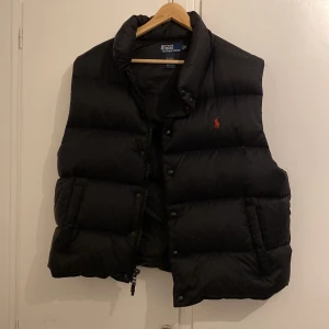 Svart dunväst från Polo Ralph Lauren - Säljer en svart dunväst från Polo Ralph Lauren. Gammal modell eftersom den har den gamla loggan. Använt fåtal gånger, köpt i USA. Väldigt bra skick och inga konstigheter. Pris kan diskuteras