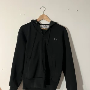 CDG Hoodie  - Säljer en svart hoodie med zip från Comme des garçons PLAY. Tröjan har hjärtat på bröstet men även ett stort på ryggen. Modellen är 185cm Perfekt för skolan eller hemma ✅🙌