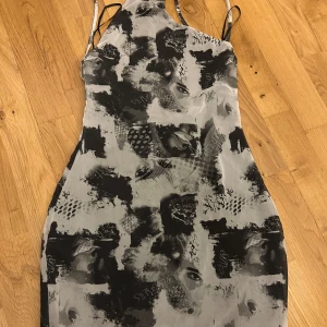 Svart och grå klänning med abstrakt mönster - Snygg klänning med ett unikt abstrakt mönster i svart och grått. Den har smala axelband och en tight passform som framhäver figuren. Perfekt för en kväll ute eller en speciell tillställning.
