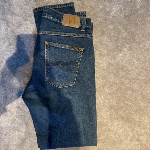 Blå nudie jeans - Snygga lean dean blå jeans från nudie med klassisk femficksdesign och orangea sömmar. De har en rak passform.