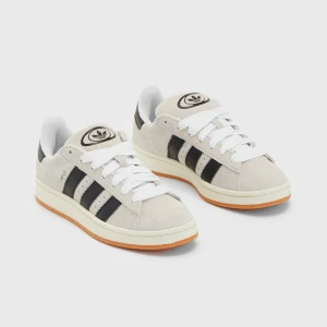 Adidas campus beige  - Snygga sneakers från Adidas i beige mocka med klassiska svarta ränder och vit sula. Skorna har en gummisula i orange och vit snörning. Perfekta för en stilren look. Campus nästan aldrig använda då dom ej passar mig 