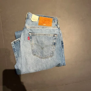 Helt nya Levi's 501 jeans med slitningar - Klassiska Levi's 501 jeans i ljusblå denim med coola slitningar på framsidan. De har en rak passform och är högmidjade, vilket ger en tidlös look. Perfekta för en avslappnad stil. Nypriss 1349 mitt endast 500.